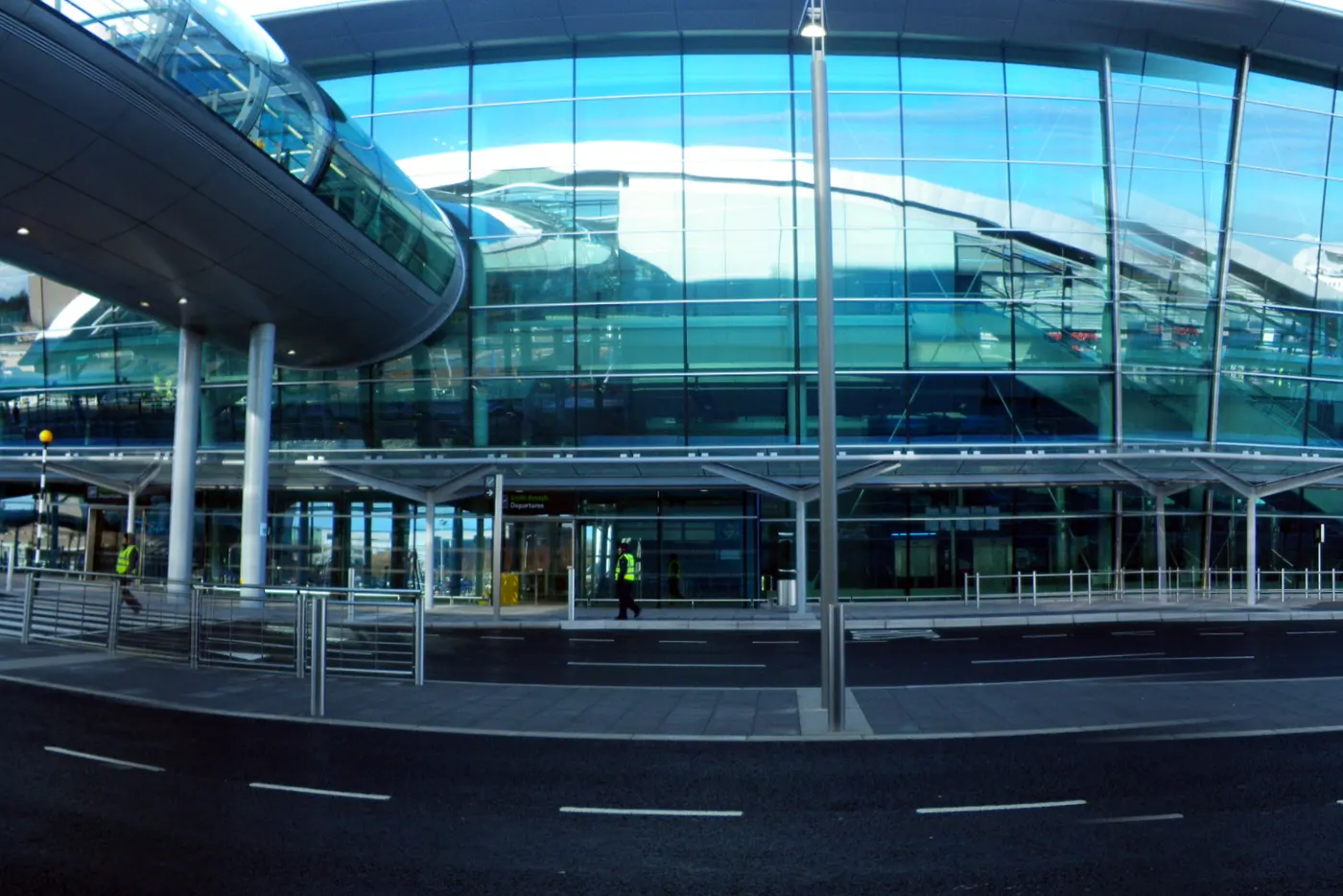 Front exterior of Dublin Airport Terminal 2, wide panoramic view of the glass facade and set-down road; a few tiny distant figures near the doors, not recognisable.